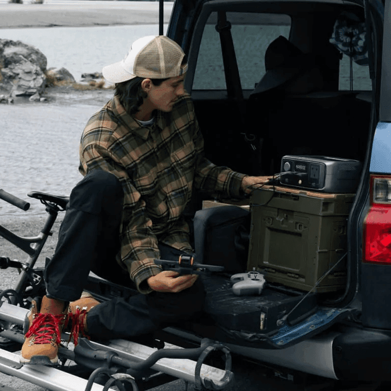 Man charging a drone using the EcoFlow River 3 Portable Power Station at the back of a vehicle during an outdoor adventure
